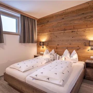 A cozy bedroom with two beds and modern wooden wall design. The rooms are bright and friendly with windows and discreet lighting elements.