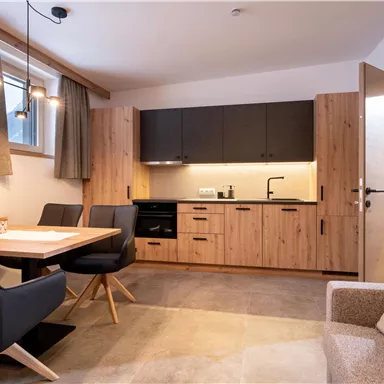 A modern kitchen unit with wooden surfaces and a dining table in a bright room. The room has large windows and an inviting atmosphere.