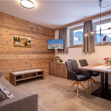 A modern living and dining room with wooden walls. There is a dining area with a table and chairs, as well as a cozy couch.