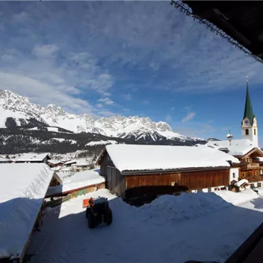 A picturesque village in the snow with impressive mountains in the background. The church with the green tower adds a charming touch.