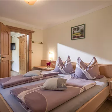 A cozy bedroom with two beds and a warm color tone. The decor is simple and welcoming, with natural light brightening the room.