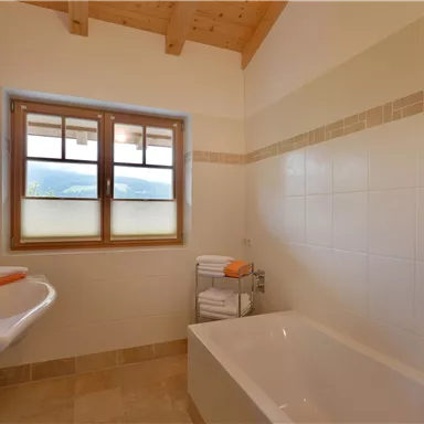 Ein modernes Badezimmer mit einer Badewanne und einem Waschbecken. Große Fenster sorgen für viel Tageslicht.