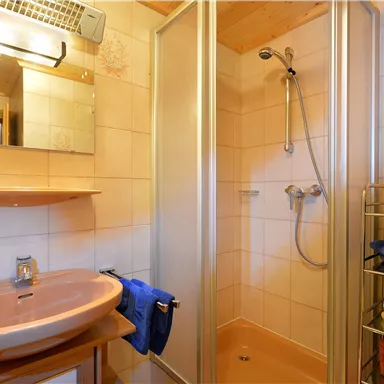 Ein modernes Badezimmer mit einer Dusche und einem Waschbecken. Handtücher in verschiedenen Farben sind ordentlich verstaut.