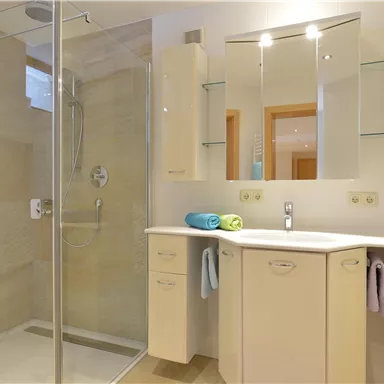 A modern bathroom with a glass shower and an elegant sink. The walls are light and there are colorful towels on the sink.