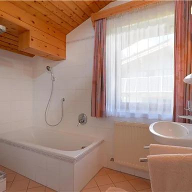 Ein helles Badezimmer mit einem Fenster, einer Badewanne und einer Dusche. Die Holzdecke verleiht dem Raum eine gemütliche Atmosphäre.