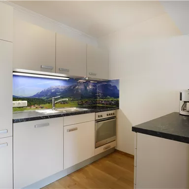 Eine moderne Küche mit hellen Schränken und einem schönen Landschaftsbild hinter dem Herd. Der Boden ist aus Holz, und auf dem Tisch stehen frische Blumen.