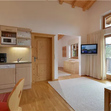 Ein gemütlicher Wohnraum mit einer modernen Küche und großen Fenstern. Helle Möbel sorgen für eine einladende Atmosphäre.