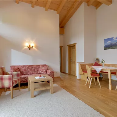 Ein gemütlicher Wohnraum mit hohen Decken und Holzdetails. Er hat eine Sitzecke mit einem Sofa und einen Esstisch mit Stühlen.