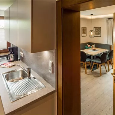 A modern kitchen with a sink and a coffee machine. In the background, an inviting dining area can be seen.