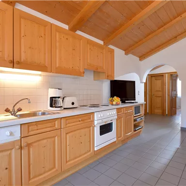 Eine moderne Küche mit Holzschränken und einem hellen, offenen Raum. In der Ecke befindet sich ein gemütlicher Sessel und die Ausstattung ist funktional.