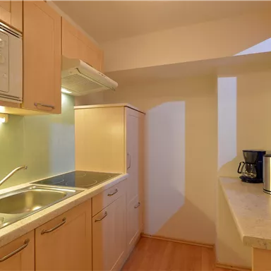 Eine moderne Küche mit Holzschränken und einer Arbeitsfläche. Sie verfügt über eine Spüle, einen Mikrowellenherd und eine Kaffeemaschine.