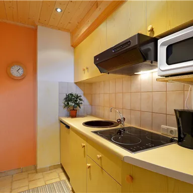 Eine moderne Küche mit gelben Möbeln und einer gemütlichen Atmosphäre. Es gibt einen Herd, eine Mikrowelle und eine Kaffeekanne sowie eine kleine Pflanze auf der Ablage.