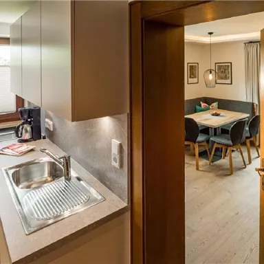 A modern kitchen with a sink and a coffee machine. In the background, an inviting dining area can be seen.