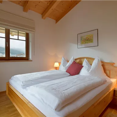 Ein gemütliches Schlafzimmer mit einem Doppelbett und einer warmen Holzdecke. Das Zimmer hat ein Fenster mit Blick auf die Landschaft und eine angenehme Beleuchtung.