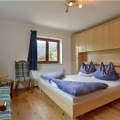 A cozy bedroom with a large bed and two comfortable chairs. Bright colors and hardwood floors create an inviting atmosphere.