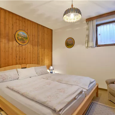 A cozy bedroom with wood paneling and a double bed. A comfortable sitting area and natural light sources create an inviting atmosphere.