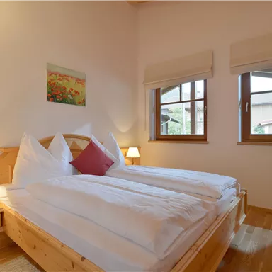 Ein gemütliches Schlafzimmer mit einem Doppelbett und holzverkleideten Wänden. Die Fenster lassen viel Tageslicht herein und schaffen eine einladende Atmosphäre.