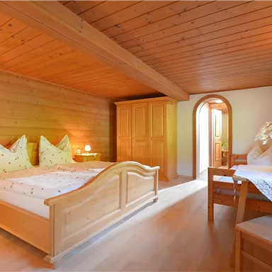 Ein gemütliches Schlafzimmer mit Holzwänden und einem Doppelbett. Es gibt einen Tisch mit Stühlen und viel natürliches Licht.