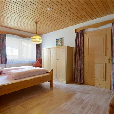 Ein gemütliches Schlafzimmer mit einem Holzbett und einer Ecke zum Entspannen. Große Fenster bringen viel Licht herein, und die Einrichtung ist einfach und stilvoll.