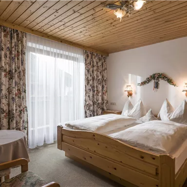 Ein gemütliches Schlafzimmer mit Holzvertäfelung und zwei Einzelbetten. Vorhänge mit floralen Mustern und ein kleiner Tisch runden das Ambiente ab.