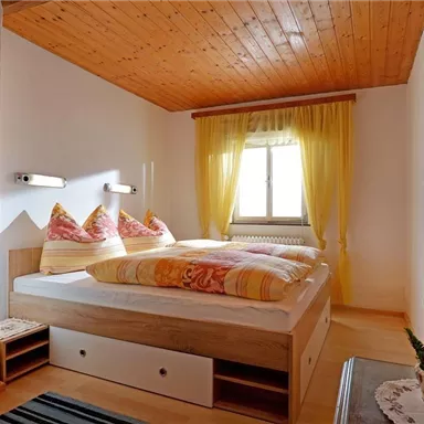 Ein gemütliches Schlafzimmer mit zwei Betten und bunten Kissen. Das Fenster lässt viel Tageslicht herein und die Vorhänge sind hell und freundlich.