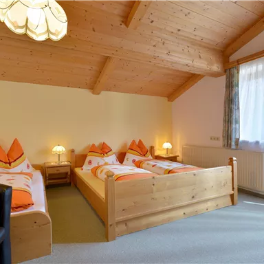 Ein gemütliches Schlafzimmer mit drei Betten aus Holz und einer warmen Holzdecke. Die Fenster lassen viel Licht herein und sorgen für eine angenehme Atmosphäre.