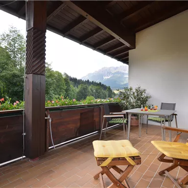 Ein gemütlicher Balkon mit zwei gelben Stühlen und einem Tisch. Im Hintergrund sind Bäume und Berge zu sehen.