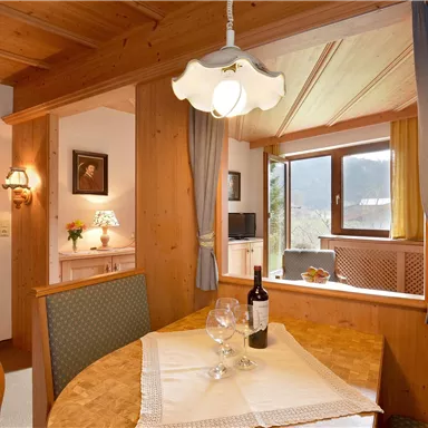 Ein gemütlicher Essbereich mit Holzmöbeln und einer warmen Atmosphäre. Durch das Fenster hat man einen Blick auf die Berge.