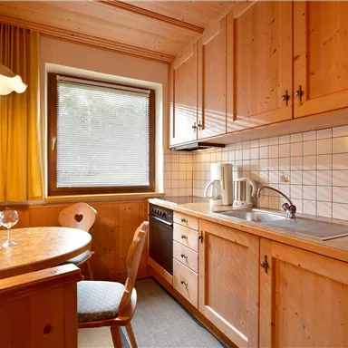 Eine gemütliche Küchenzeile aus Holz mit einem runden Tisch und einem Fenster. Auf dem Tisch stehen Weingläser und eine Schale mit Äpfeln.