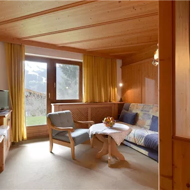 Ein gemütlicher Wohnraum mit Holzverkleidung und großen Fenstern. Das Zimmer ist hell und freundlich, mit einem Sofa, Stühlen und einem kleinen Tisch.