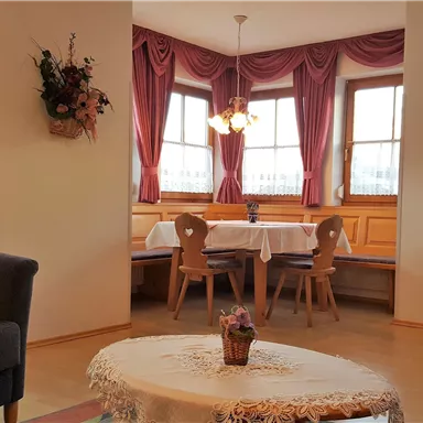 Ein gemütlicher Wohnbereich mit einem grauen Sofa und einem runden Tisch. Der Raum hat große Fenster mit Vorhängen und eine einladende Sitzecke.