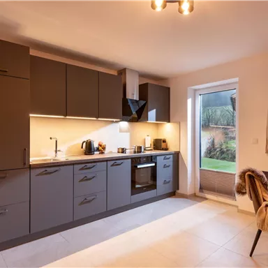 A modern kitchen with gray cabinets and a bright workspace. Daylight comes through the window and there is a view of the garden.