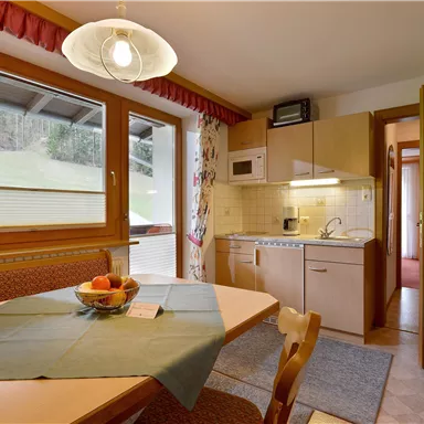 A cozy kitchen with a round table and fruit bowl. Large windows provide plenty of light and a view of the outdoors.