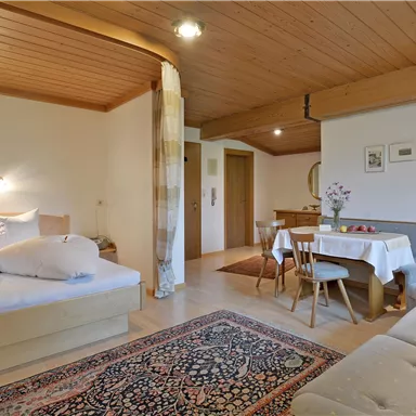 A cozy room with a double bed, a seating area, and a dining area. The room has a warm, inviting ambiance.