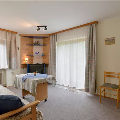 Ein gemütliches Wohnzimmer mit einem Sofa und einem Tisch. Große Fenster sorgen für viel Tageslicht.