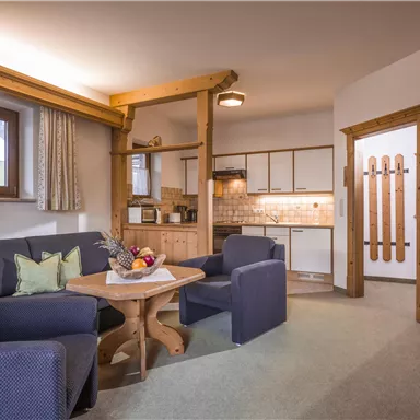 Ein gemütliches Wohnzimmer mit blauen Sesseln und einem Holztisch. Die offene Küche ist modern und freundlich eingerichtet.