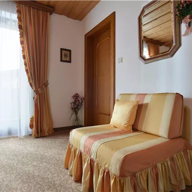 Ein gemütlicher Bereich mit einem gepolsterten Sessel und einem großen Fenster. Der Raum ist hell und freundlich mit einem warmen Farbton.