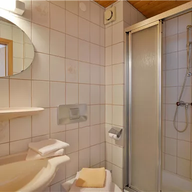 Ein modernes Badezimmer mit einer Dusche und einem Waschbecken. Die Wände sind hell gefliest und es gibt einen runden Spiegel.