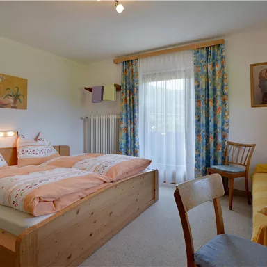 Ein gemütliches Schlafzimmer mit einem Doppelbett und hellen Dekorationen. Ein kleiner Tisch und eine Couch runden die entspannte Atmosphäre ab.