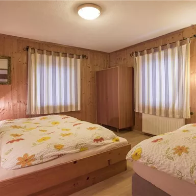 A cozy bedroom with wooden paneling and two beds. The walls are decorated with matching curtains and a mirror.