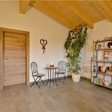 An inviting room with a wooden ceiling and tiled floor. A small seating area with a table and two chairs, as well as a bookshelf, adds coziness to the space.