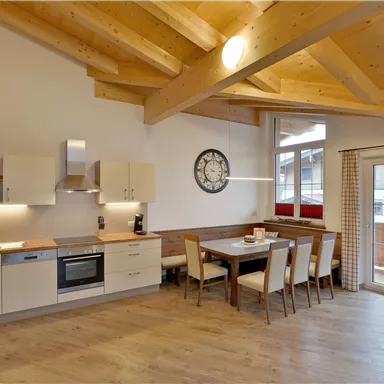 A modern kitchen unit with wooden beam ceiling and a dining area. Bright colors and plenty of natural light create an inviting atmosphere.