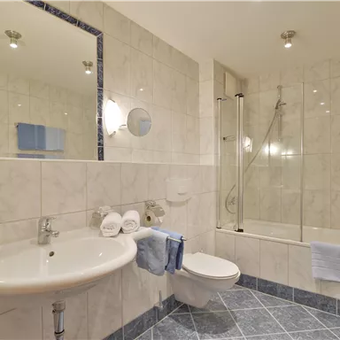 Ein modernes Badezimmer mit einer Dusche und Badewanne. Die Wände sind in hellem Marmor gehalten, mit einem großen Spiegel und sanfter Beleuchtung.