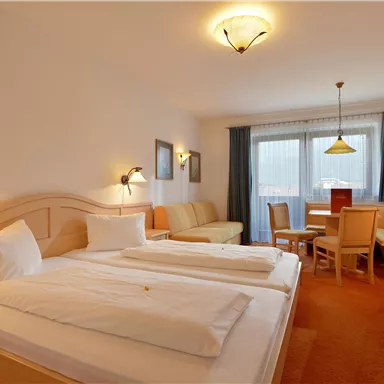 Ein gemütliches Hotelzimmer mit zwei Einzelbetten und einem kleinen Wohnbereich. Große Fenster sorgen für viel Tageslicht.