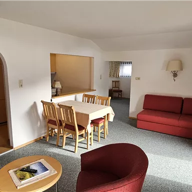 A bright living room with a red sofa and a dining table. The atmosphere is cozy and inviting.