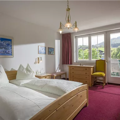 Ein helles Zimmer mit zwei Einzelbetten und einem Schreibtisch. Große Fenster bieten einen Blick auf die Landschaft draußen.