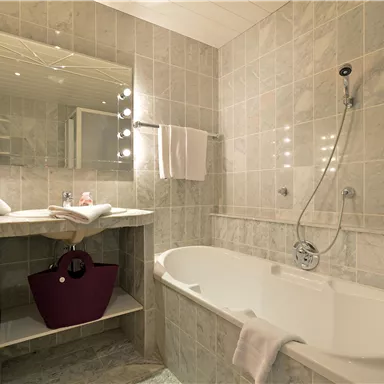 Ein modernes Badezimmer mit einer Badewanne und einem Waschtisch. Helle Fliesen und große Spiegel verleihen dem Raum eine elegante Atmosphäre.