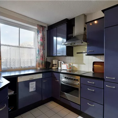 Eine moderne Küche mit blauen Schränken und einer Edelstahl-Spüle. Das Fenster lässt viel Tageslicht herein.