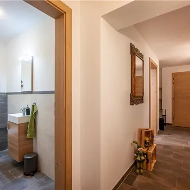 A bright hallway with wooden paneling and modern bathrooms. To the right, doors lead to additional rooms that create an inviting atmosphere.
