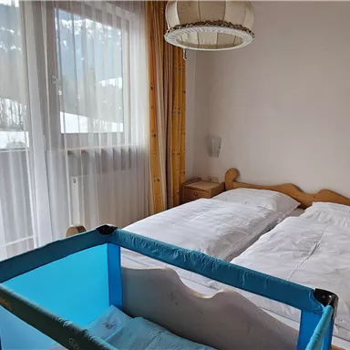 A bright bedroom with two beds and a crib. Large windows let in a lot of light.